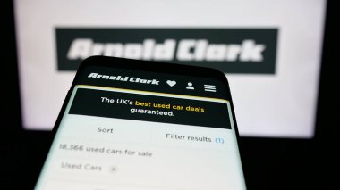 Stuttgart, Almanya - 03-04-2025: Araba satıcısı şirketi Arnold Clark Automobiles Ltd. 'nin logosunu içeren cep telefonu iş sitesinin önünde ekranda. Telefon ekranının sol üst kısmına odaklan.