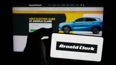 Stuttgart, Almanya - 03-04-2025: Araba satıcısı Arnold Clark Automobiles Ltd. 'nin logosu olan cep telefonu sahibi kişi iş sayfasının önünde ekranda. Telefon ekranına odaklan.