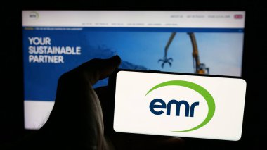 Stuttgart, Almanya - 03-04-2025: İngiliz Avrupa Metal Geri Dönüşüm Limited (EMR) şirketinin logosuna sahip cep telefonu sahibi kişi iş sayfasının önünde ekranda görülüyor. Telefon ekranına odaklan.