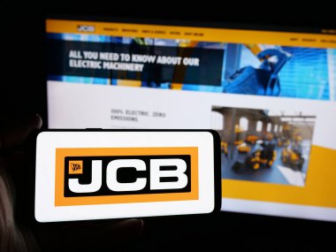 Stuttgart, Almanya - 03-04-2025: İngiliz J.C. Bamford Excavators Limited (JCB) şirketinin logosuna sahip kişi iş sitesinin önünde ekranda görülüyor. Telefon ekranına odaklan.