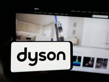 Stuttgart, Almanya - 03-04-2025: Ev aletleri şirketi Dyson Limited 'in logosuna sahip akıllı telefon sahibi kişi iş sitesinin önünde ekranda görülüyor. Telefon ekranına odaklan.