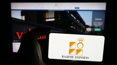 Stuttgart, Almanya - 03-13-2025: Üzerinde Hint altın şirketi Rajesh Exports Limited 'in logosu bulunan cep telefonu sahibi kişi iş sayfasının önünde ekranda görülüyor. Telefon ekranına odaklan.
