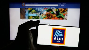 Stuttgart, Almanya - 03-13-2025: Alman perakende şirketi ALDI 'nin logosuna sahip cep telefonu sahibi kişi iş sayfasının önünde ekrana yansıdı. Telefon ekranına odaklan.