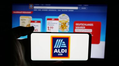 Stuttgart, Almanya - 03-13-2025: Alman perakende şirketi ALDI 'nin logosunun bulunduğu cep telefonu sahibi kişi iş sayfasının önünde ekrana yansıdı. Telefon ekranına odaklan.
