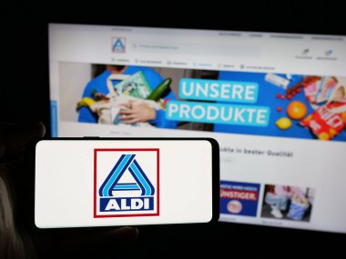 Stuttgart, Almanya - 03-13-2025: Alman ALDI Nord Deutschland Stiftung Co. KG şirketinin logosunu taşıyan kişi iş sitesinin önünde ekranda. Telefon ekranına odaklan.