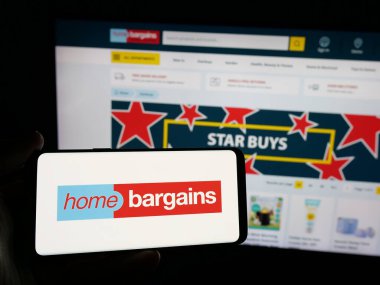 Stuttgart, Almanya - 03-13-2025: İngiliz T.J. Morris Limited (Ev Pazarlığı) şirketinin logosuna sahip kişi iş sitesinin önünde ekranda. Telefon ekranına odaklan.