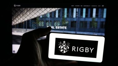 Stuttgart, Almanya - 03-13-2025: İngiliz firması Rigby Group plc 'in logosuyla cep telefonu sahibi kişi iş sayfasının önünde ekranda. Telefon ekranına odaklan.