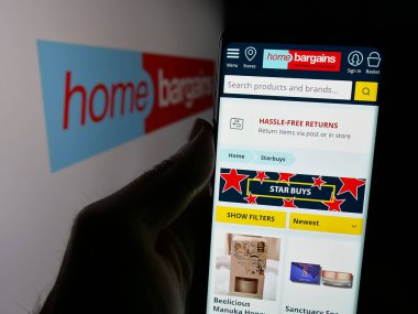 Stuttgart, Almanya - 03-13-2025: Logo önünde üzerinde İngiliz firması T.J. Morris Limited (Home Bargains) logosu bulunan kişi. Telefon ekranının merkezine odaklan.
