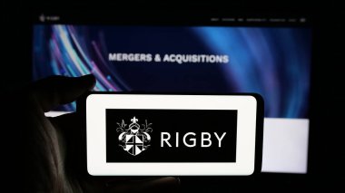 Stuttgart, Almanya - 03-13-2025: İngiliz firması Rigby Group plc 'in logosuyla cep telefonu sahibi kişi iş sayfasının önünde ekranda. Telefon ekranına odaklan.