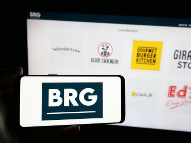 Stuttgart, Almanya - 03-13-2025: İngiliz restoran şirketi Boparan Holding Limited 'in logosunun bulunduğu akıllı telefon sahibi kişi iş sitesinin önünde ekranda görülüyor. Telefon ekranına odaklan.