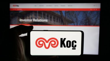 Stuttgart, Almanya - 03-13-2025: Türk sanayi şirketi Koç Holding A.S. 'nin logosuyla cep telefonu sahibi olan kişi, iş dünyasının web sayfası önünde ekranda görülüyor. Telefon ekranına odaklan.