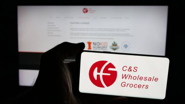 Stuttgart, Almanya - 03-06-2025: ABD 'li firma CS Toptan Bakkal LLLC (CSWG) logosuna sahip cep telefonu sahibi kişi iş sayfasının önünde ekranda görülüyor. Telefon ekranına odaklan.