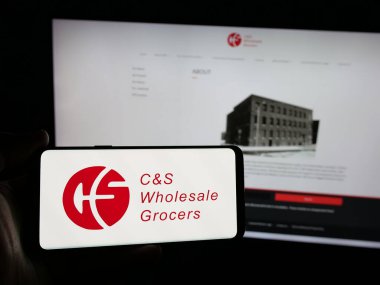 Stuttgart, Almanya - 03-06-2025: ABD 'li CS Toptan Bakkal LLLC (CSWG) şirketinin logosuna sahip kişi iş sitesinin önünde ekranda görülüyor. Telefon ekranına odaklan.