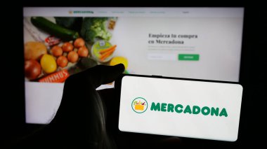Stuttgart, Almanya - 03-06-2025: Üzerinde İspanyol süpermarket şirketi Mercadona S.A. 'nın logosu olan cep telefonu sahibi kişi iş sayfasının önünde ekranda. Telefon ekranına odaklan.