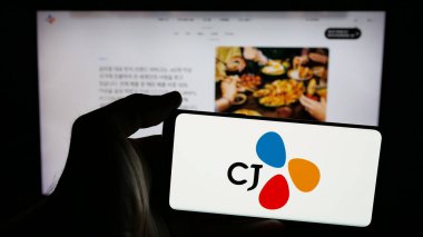 Stuttgart, Almanya - 03-06-2025: Güney Koreli şirket CJ Corporation 'ın logosuyla cep telefonu sahibi kişi iş sayfasının önünde ekranda. Telefon ekranına odaklan.