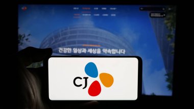 Stuttgart, Almanya - 03-06-2025: Güney Koreli CJ Corporation şirketinin logosuyla cep telefonu sahibi kişi iş sayfasının önünde ekranda. Telefon ekranına odaklan.