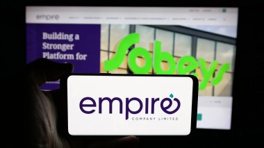 Stuttgart, Almanya - 03-06-2025: Kanadalı Empire Company Limited şirketinin logosuyla cep telefonu sahibi kişi iş sayfasının önünde ekranda. Telefon ekranına odaklan.