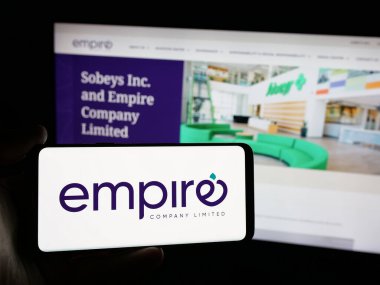 Stuttgart, Almanya - 03-06-2025: Kanadalı Empire Company Limited şirketinin logosuna sahip kişi iş sitesinin önünde ekranda. Telefon ekranına odaklan.