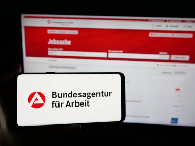 Stuttgart, Almanya - 03-07-2025: Alman federal ajansı Bundesagentur fuer Arbeit 'in logosunun bulunduğu akıllı telefonu web sitesinin önünde tutan kişi. Telefon ekranına odaklan.