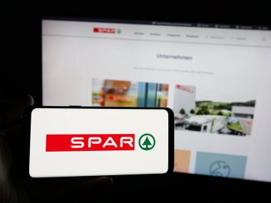 Stuttgart, Almanya - 03-07-2025: İsviçreli perakende firması SPAR Holding AG 'nin logosunu taşıyan kişi iş sitesinin önünde ekranda. Telefon ekranına odaklan.