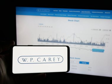 Stuttgart, Almanya - 03-07-2025: ABD 'li emlak şirketi W. P. Carey Inc.' in logosunu taşıyan kişi iş sitesinin önünde ekranda. Telefon ekranına odaklan.