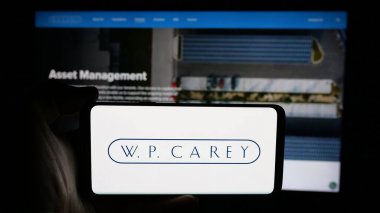 Stuttgart, Almanya - 03-07-2025: ABD 'li emlak şirketi W. P. Carey Inc.' in logosuyla cep telefonu sahibi kişi iş sayfasının önünde ekranda. Telefon ekranına odaklan.
