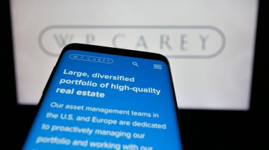 Stuttgart, Almanya - 03-07-2025: ABD 'li emlak şirketi W. P. Carey Inc.' in logosunu taşıyan cep telefonu iş sitesinin önünde ekranda. Telefon ekranının sol üst kısmına odaklan.