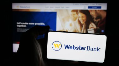 Stuttgart, Almanya - 03-07-2025: Web sayfası önünde ekranda ABD 'li finans şirketi Webster Financial Corporation' ın logosuyla cep telefonu tutan kişi. Telefon ekranına odaklan.