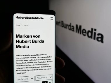 Stuttgart, Almanya - 03-07-2025: Alman Hubert Burda Media Holding KG 'nin web sayfası ile cep telefonu tutan kişi logo önünde ekranda. Telefon ekranının merkezine odaklan.