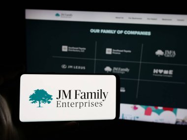 Stuttgart, Almanya - 03-09-2025: ABD 'li şirket JM Family Enterprises Inc.' in logosuna sahip akıllı telefon sahibi kişi web sitesinin önünde ekranda. (JMFE) Telefon ekranına odaklan.