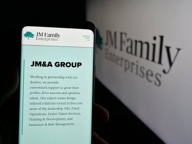 Stuttgart, Almanya - 03-09-2025: ABD 'li JM Family Enterprises Inc. (JMFE) şirketinin web sayfası logonun önünde bulunan kişi. Telefon ekranının merkezine odaklan.