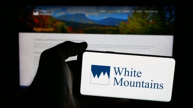 Stuttgart, Almanya - 03-09-2025: White Mountains Sigorta Grubu Ltd. şirketinin logosuna sahip cep telefonu sahibi kişi web sayfasının önünde ekranda. Telefon ekranına odaklan.