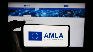 Stuttgart, Almanya - 03-10-2025: Web sayfası önünde ekranda Anti-Para Aklama Kurumu (AMLA) logosu bulunan kişi. Telefon ekranına odaklan.