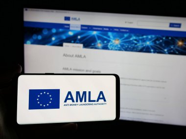 Stuttgart, Almanya - 03-10-2025: Web sitesi önünde ekranda Anti-Para Aklama Kurumu (AMLA) logosu bulunan kişi. Telefon ekranına odaklan.