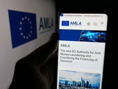 Stuttgart, Almanya - 03-10-2025: Logo önünde ekranda Anti-Para Aklama Kurumu (AMLA) web sayfası bulunan kişi. Telefon ekranının merkezine odaklan.