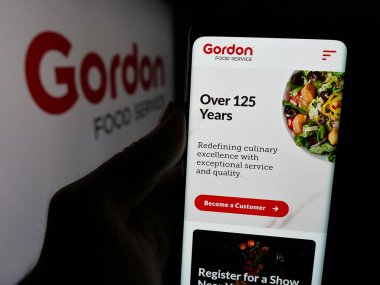 Stuttgart, Almanya - 03-10-2025: Logonun önünde üzerinde ABD 'li Gordon Food Service Inc. (GFS) şirketinin logosu bulunan kişi. Telefon ekranının merkezine odaklan.
