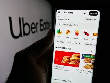 Stuttgart, Almanya - 03-12-2025: ABD 'li çevrimiçi gıda dağıtım şirketi Uber Eats' in internet sayfası ile cep telefonu tutan kişi logonun önünde ekranda. Telefon ekranının merkezine odaklan.