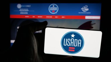 Stuttgart, Almanya - 03-12-2025: İnternet sayfası önünde ABD Anti-Doping Ajansı (USADA) logosu olan cep telefonu sahibi kişi. Telefon ekranına odaklan.