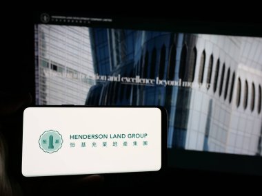 Stuttgart, Almanya - 03-14-2025: Henderson Arazi Geliştirme Şirketi 'nin logosuna sahip akıllı telefon sahibi kişi web sitesinin önünde ekranda. Telefon ekranına odaklan.