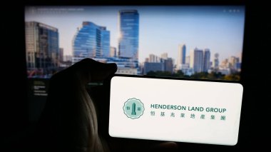 Stuttgart, Almanya - 03-14-2025: Henderson Arazi Geliştirme Şirketi logosu olan cep telefonu sahibi kişi web sayfasının önünde ekranda. Telefon ekranına odaklan.
