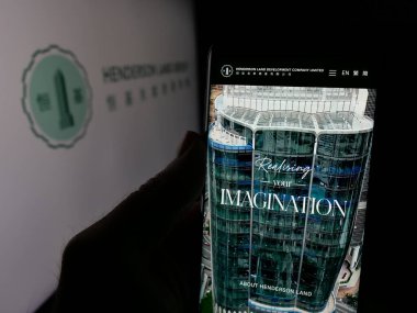 Stuttgart, Almanya - 03-14-2025: Henderson Arazi Geliştirme Şirketi Ltd. 'nin web sayfası ile logonun önünde cep telefonu tutan kişi. Telefon ekranının merkezine odaklan.