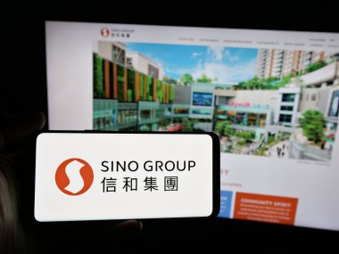Stuttgart, Almanya - 03-14-2025: Web sitesi önünde ekranda Hong Kong emlak şirketi Sino Group 'un logosunun bulunduğu akıllı telefonu tutan kişi. Telefon ekranına odaklan.