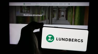 Stuttgart, Almanya - 03-14-2025: Web sayfası önünde üzerinde L E Lundbergforetagen AB (Lundbergs) şirketinin logosu bulunan cep telefonu sahibi kişi. Telefon ekranına odaklan.