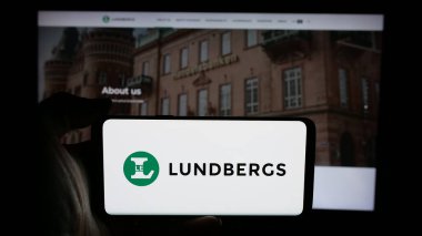 Stuttgart, Almanya - 03-14-2025: Web sayfası önünde, üzerinde L E Lundbergforetagen AB (Lundbergs) şirketinin logosu bulunan cep telefonu sahibi kişi. Telefon ekranına odaklan.