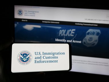 Stuttgart, Almanya - 03-18-2025: İnternet sitesi önünde üzerinde ABD Göçmenlik ve Gümrük Muhafaza Teşkilatı (ICE) logosu bulunan akıllı telefon sahibi kişi. Telefon ekranına odaklan.
