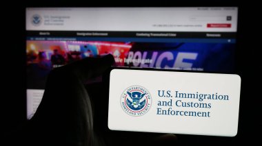 Stuttgart, Almanya - 03-18-2025: İnternet sayfası önünde üzerinde ABD Göçmenlik ve Gümrük Uygulaması (ICE) logosu bulunan cep telefonu sahibi kişi. Telefon ekranına odaklan.