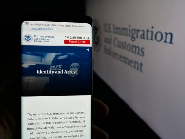 Stuttgart, Almanya - 03-18-2025: ABD Göçmenlik ve Gümrük Muhafaza Teşkilatı (ICE) web sitesi logosu önünde cep telefonu tutan kişi. Telefon ekranının merkezine odaklan.