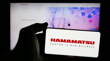 Stuttgart, Almanya - 03-18-2025: Japon şirketi Hamamatsu Photonics K.K. logosuna sahip cep telefonu sahibi kişi Web sayfasının önünde ekranda. Telefon ekranına odaklan.