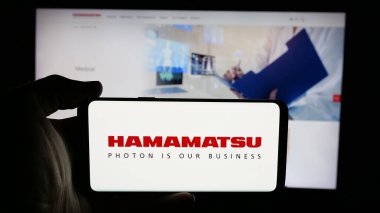 Stuttgart, Almanya - 03-18-2025: Japon şirketi Hamamatsu Photonics K.K. logosuyla cep telefonu tutan kişi Web sayfasının önünde ekranda. Telefon ekranına odaklan.