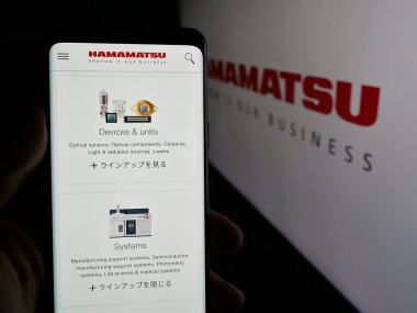 Stuttgart, Almanya - 03-18-2025: Japon şirketi Hamamatsu Photonics K.K. 'nin web sayfası ile cep telefonu tutan kişi Ekranda logonun önünde. Telefon ekranının merkezine odaklan.